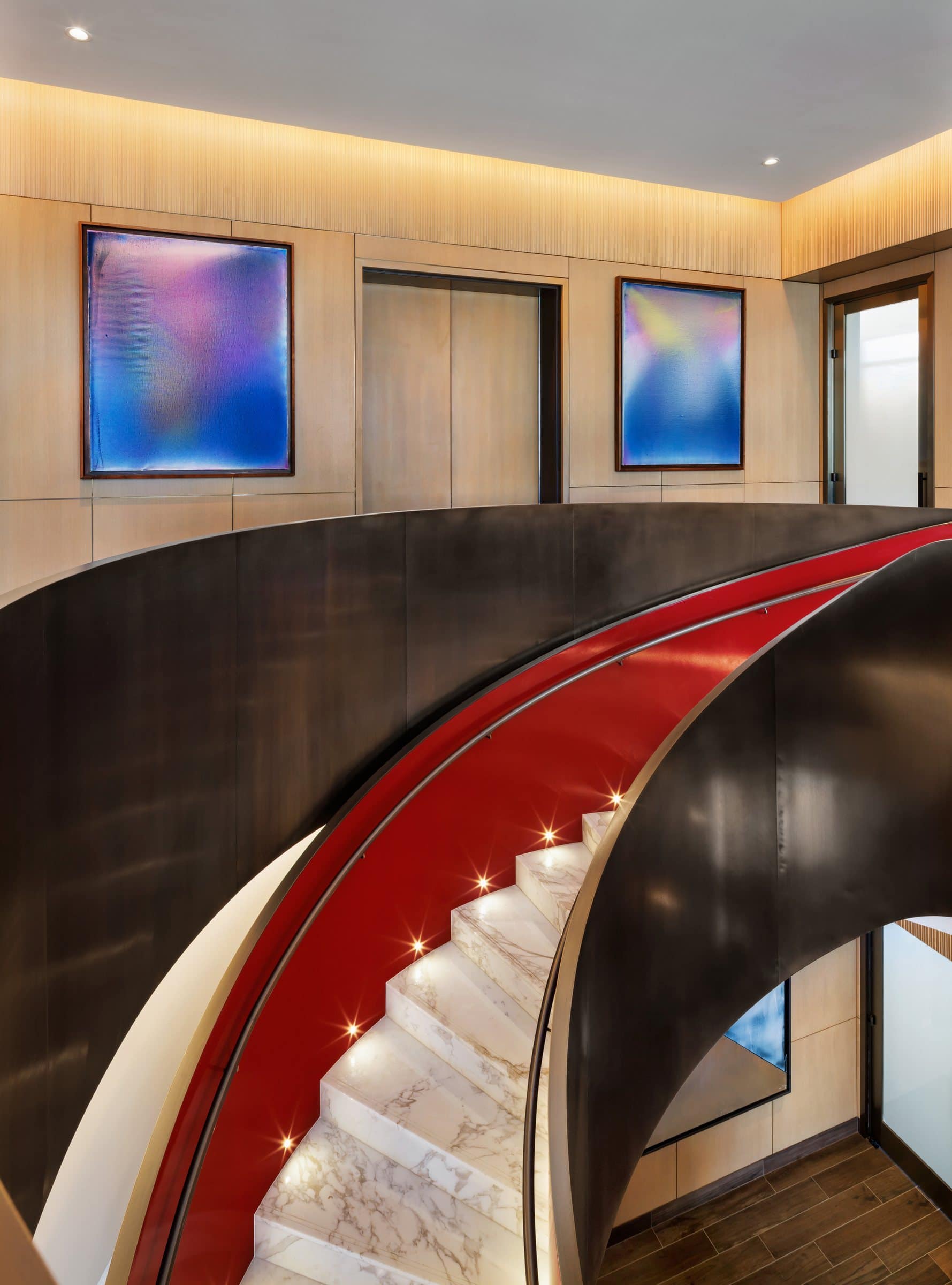 Red-lined spiral stair rising toward two blue, violet and pink gradient paintings on wood-paneled walls