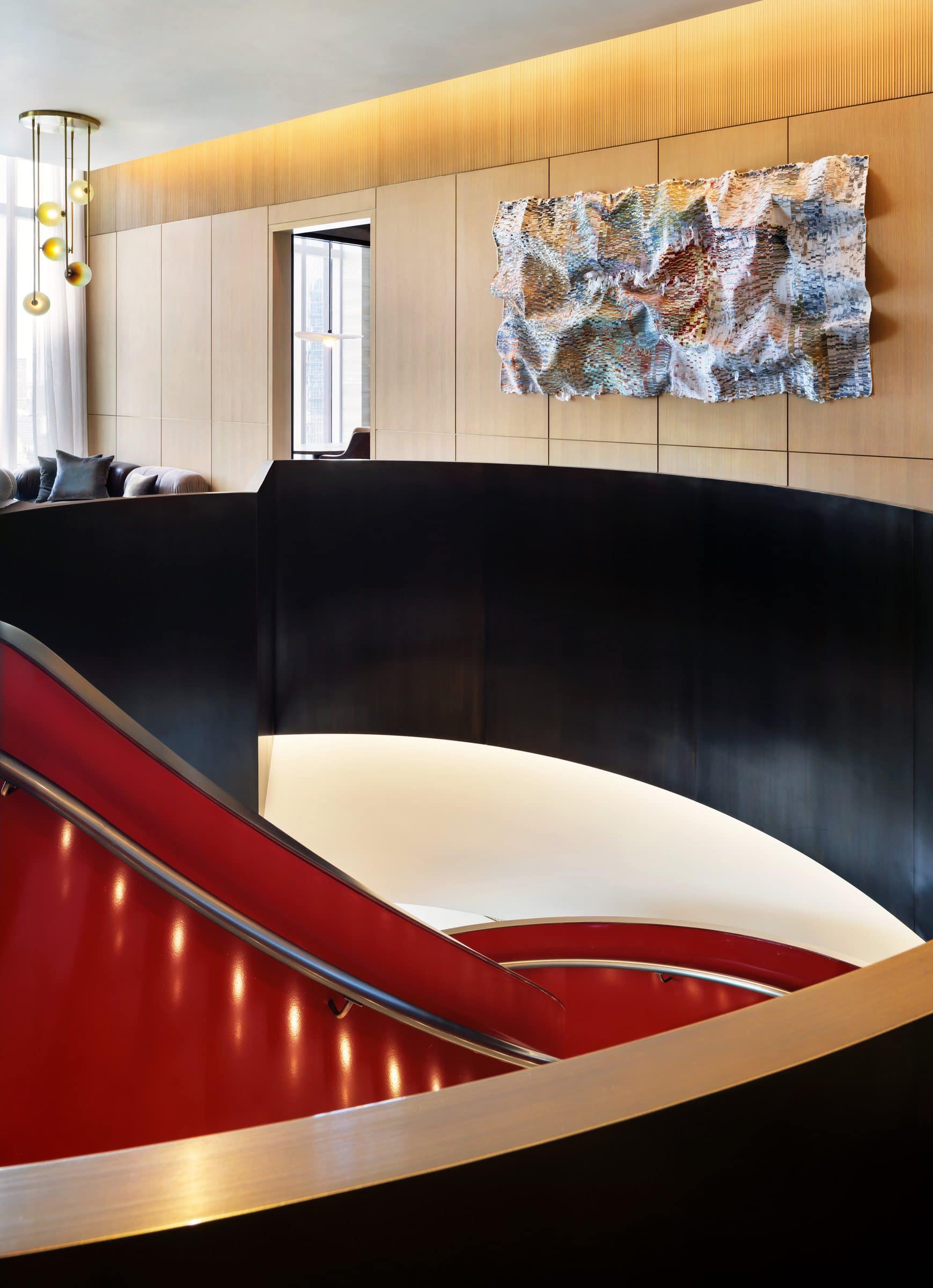 Large rippling blue, ochre and white textile work on a lounge wall beyond a red-lined spiral stair