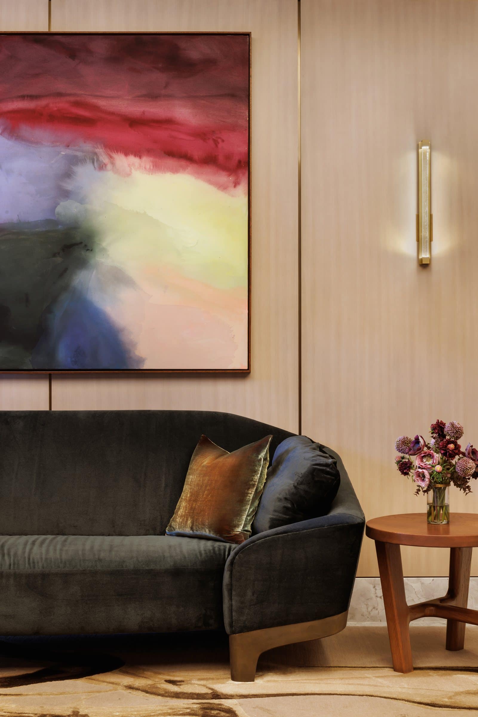Dark curved sofa beneath a painting of red, gray, yellow and blue color washes