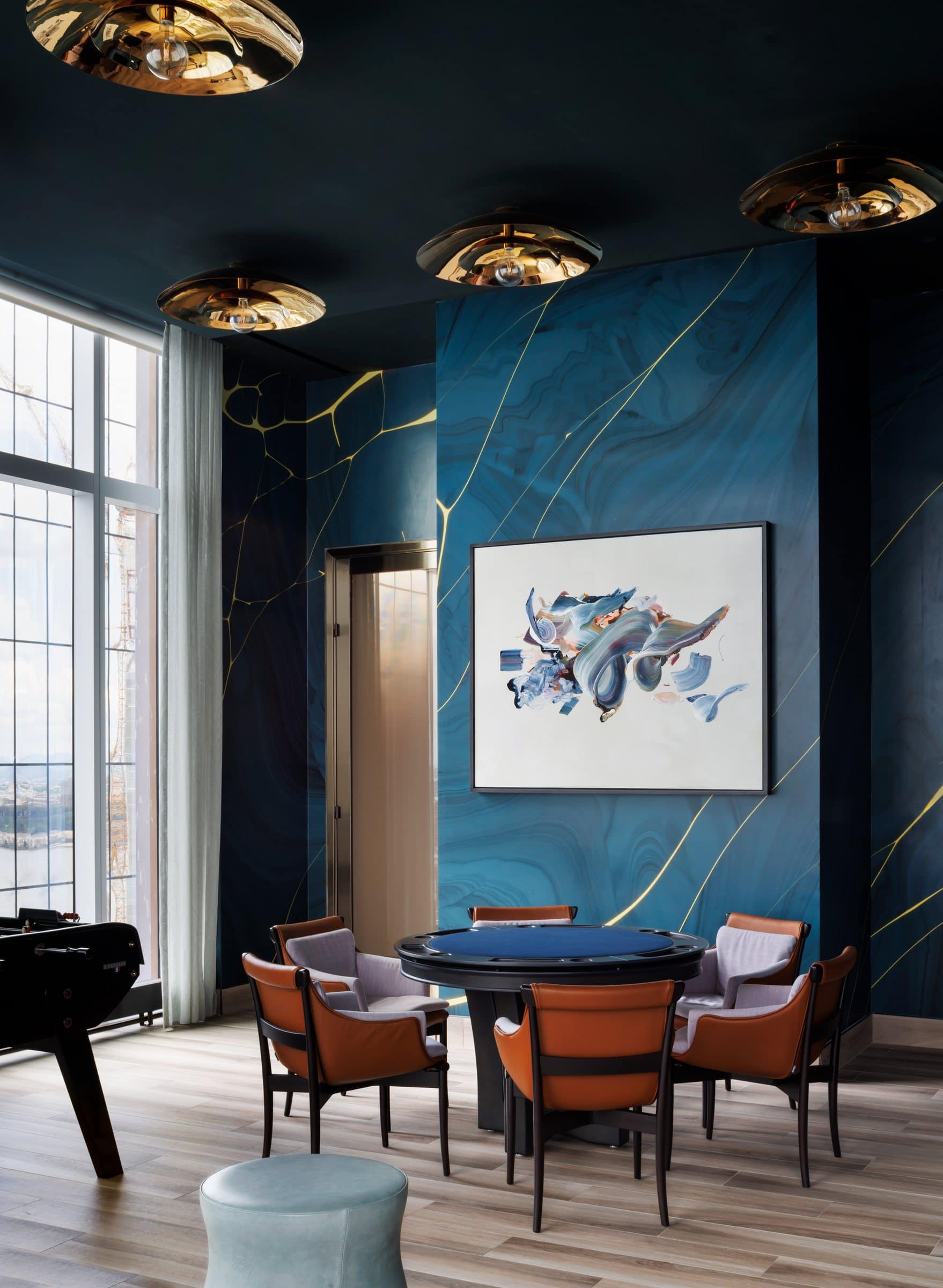 Small round table and leather chairs beneath a blue, gray and white gestural painting in a dark teal lounge