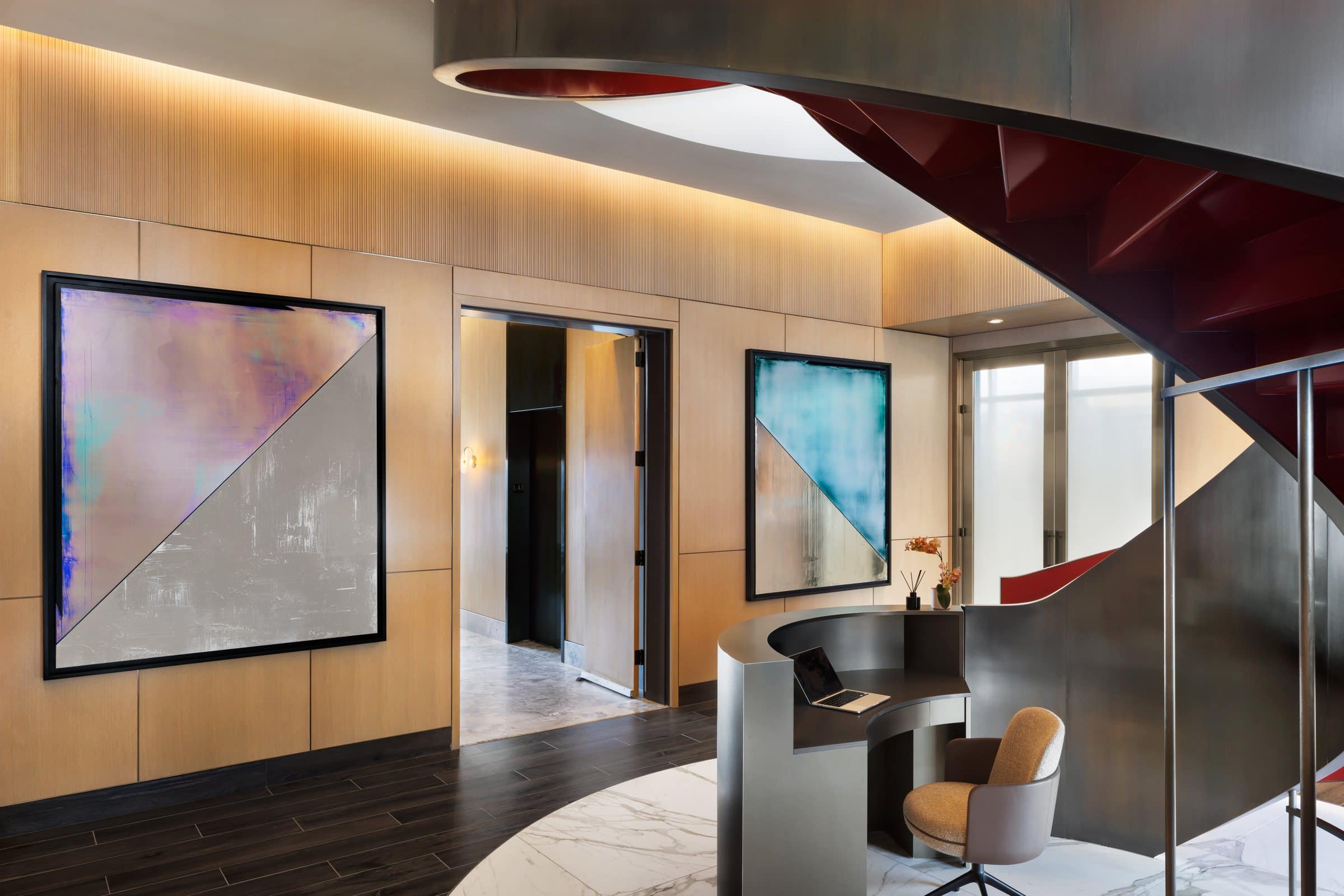 Two large silver canvases with lavender and teal triangular fields flank a doorway beside a curved desk and spiral stair