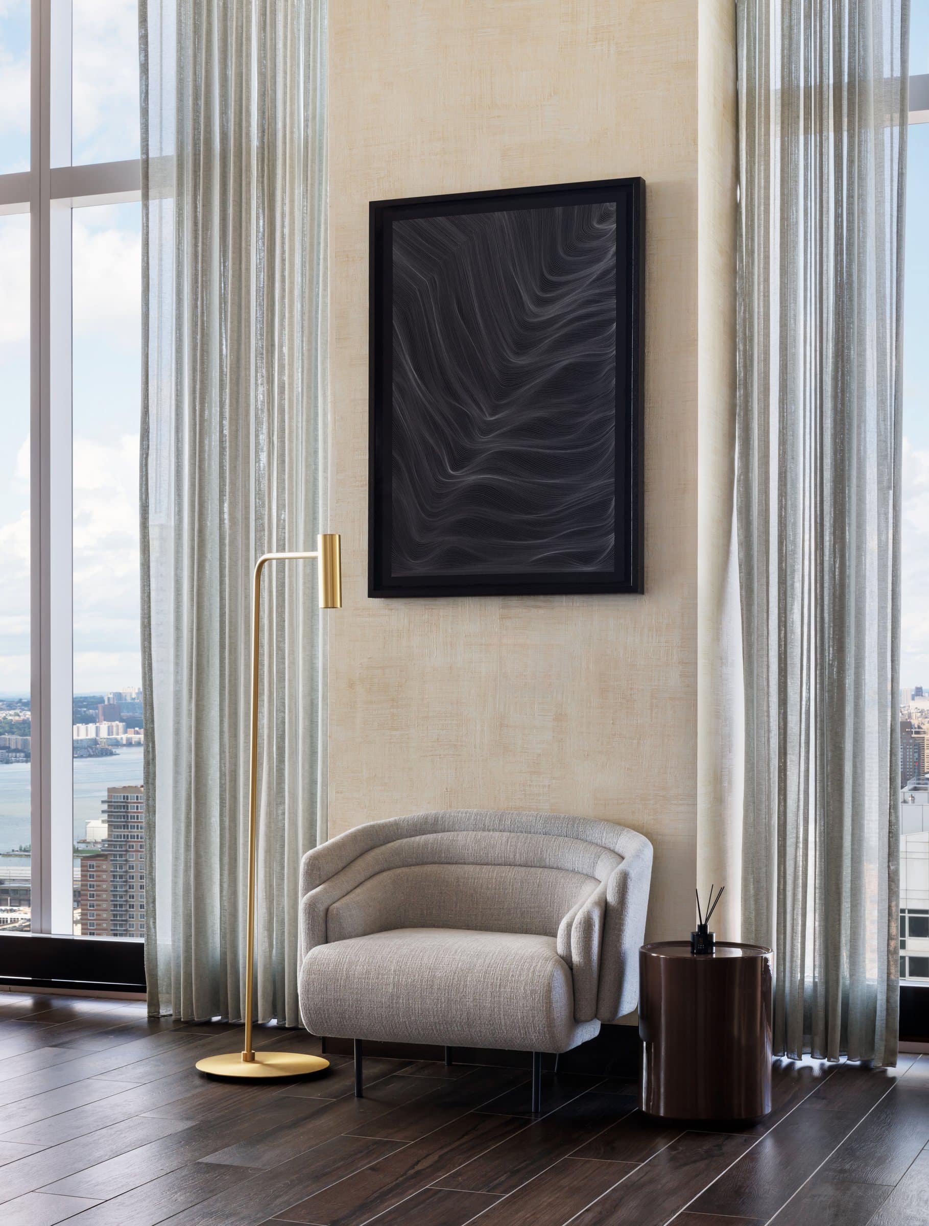 Pale armchair beneath a black-framed work of fine undulating white lines on black